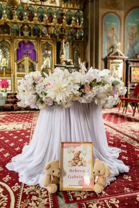 Masa de botez din biserică, cu flori albe și numele Rebeca Gabriela