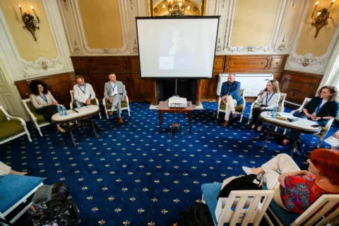 Dezbatere într-un salon istoric, cu invitații așezați în cerc și prezentarea pe ecran