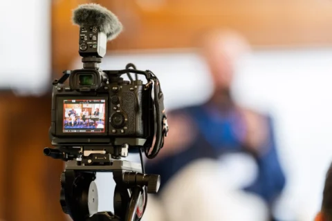 Cameră video pe trepied filmând o conferință