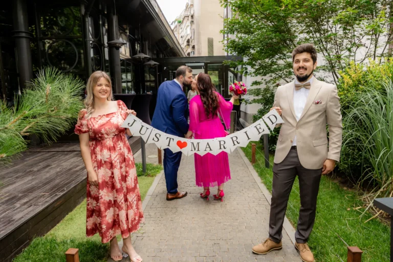 Prietenii țin bannerul „Just married” în timp ce mirii se sărută pe alee