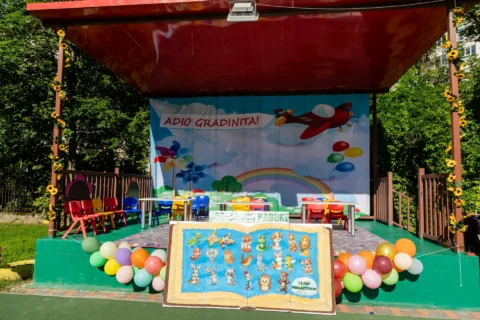Scena decorată pentru serbarea „Adio, grădiniță!”, cu baloane colorate și o carte uriașă