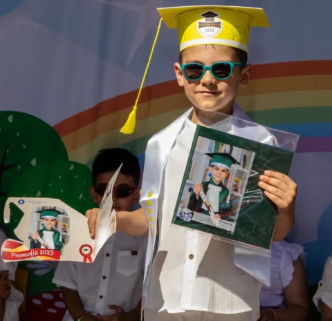 Băiețel cu tichie de absolvent arătând diploma și fotografia lui