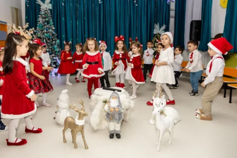 Copii în costume roșii dansând în jurul decorului de iarnă, la serbarea de Crăciun