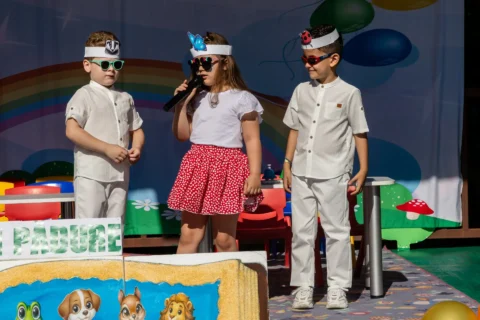 Trei copii cu ochelari de soare prezentând serbarea de absolvire a grădiniței