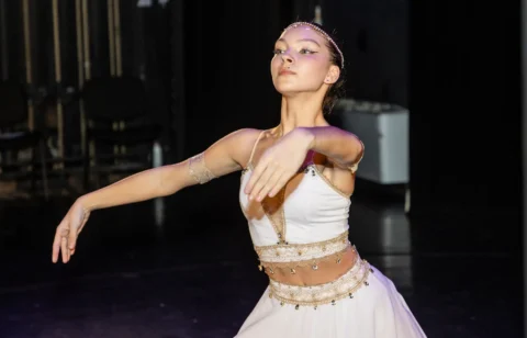Prim-plan cu o tânără balerină în costum alb, în lumina scenei