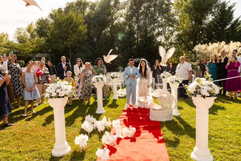 Ceremonie în grădină, cu mirii pe covorul roșu între invitați