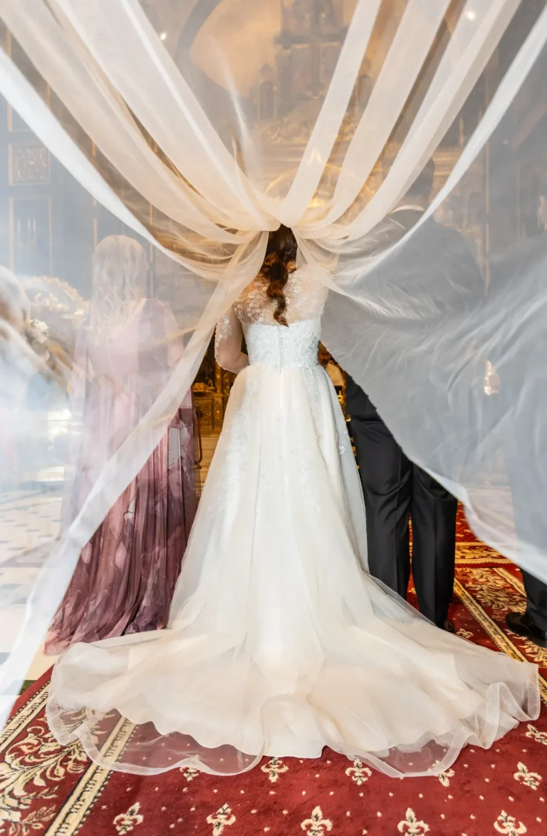 Mireasa văzută din spate, între draperii albe, cu trena întinsă