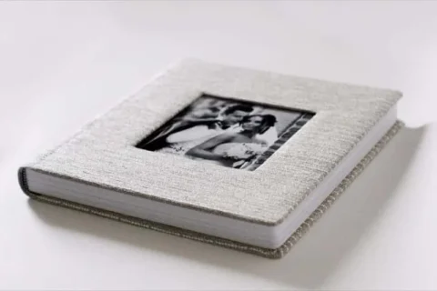 Fotocarte de nuntă cu copertă textil gri deschis și fotografia mirilor într-o fereastră decupată