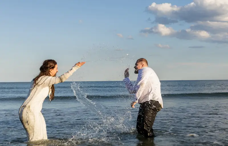 Mireasa și mirele se stropesc cu apă în mare, ședință trash the dress